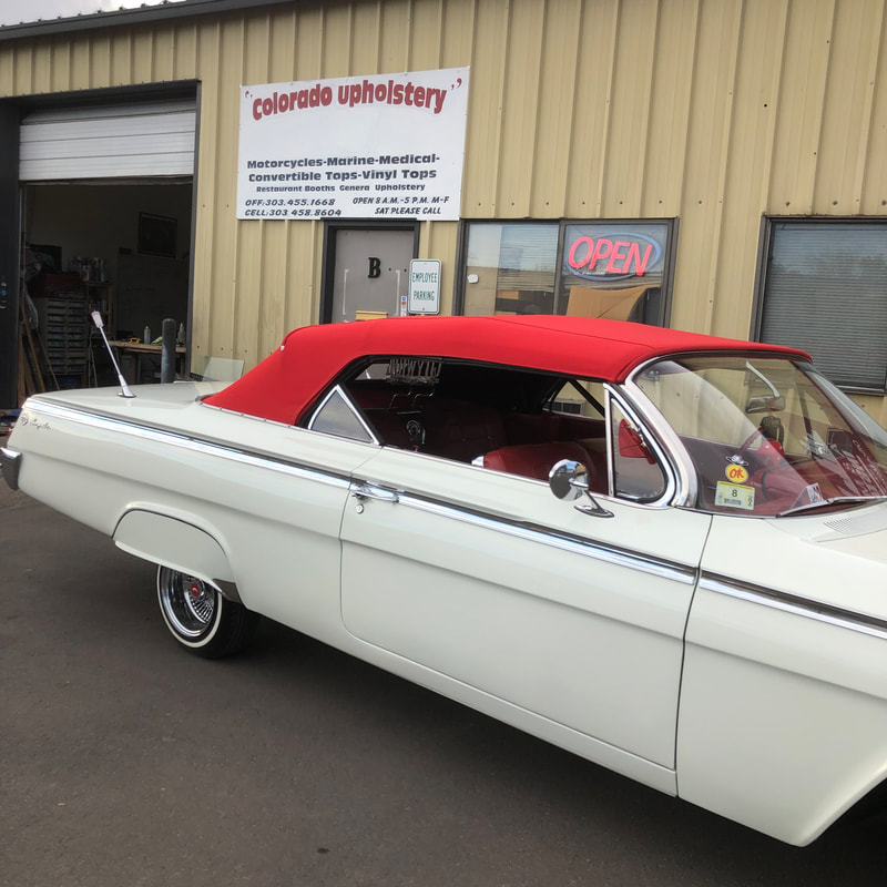 White classic car with a finished red top parked outside the Colorado Upholstery workshop sign